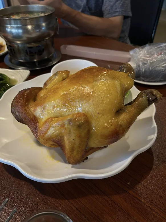 A whole golden roast chicken on a white plate at a round table set for a family meal in Taiwan